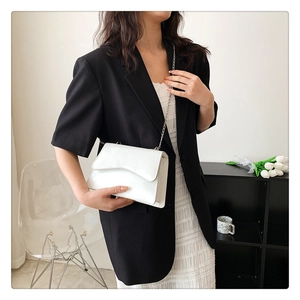 Detailed view of white crossbody flap bag with wavy edges and silver chain strap