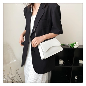 Detail of white patent leather shoulder bag with unique wavy flap and silver chain strap