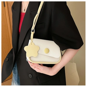 Detail of a creamy white crossbody bag with yellow flower charm on a black blazer outfit