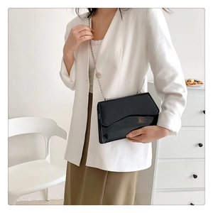 Model wearing a black patent leather crossbody bag with geometric asymmetrical flap and chain
