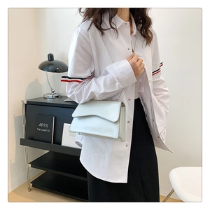 Chic off-white patent leather flap crossbody bag with silver chain strap worn by model
