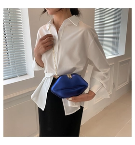 Détail d'un sac à main bleu roi en forme de lèvres avec une chaîne dorée sur un mannequin