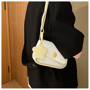 Close-up of a white leather saddle bag with yellow trim and flower charm on a model