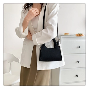 Detail of minimalist black crossbody bag paired with a white blazer and brown skirt
