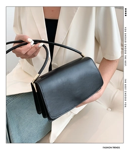 Detail of minimalist black leather shoulder bag with gold hardware and flap closure