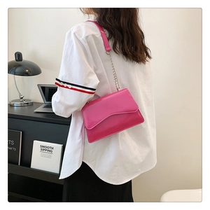 Detail of fuchsia patent leather crossbody bag with chain strap and wave flap design