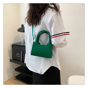 Detail view of a bright green felt handbag shown on model in a modern interior setting