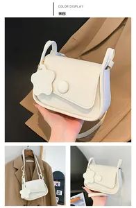 Detail view of off-white crossbody bag featuring round buckle and floral charm
