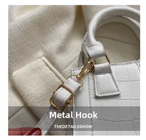Detailed macro view of golden hardware hook on white crocodile embossed leather bag