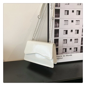 Close-up of a white glossy crossbody bag with scalloped flap and silver chain strap