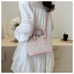 Détail du sac coquille tissé beige avec bandoulière en cuir rose sur l'épaule