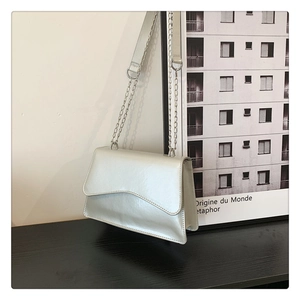Detail of silver metallic crossbody bag with wave flap edge and silver chain strap