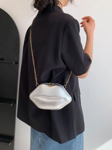 Sac à bandoulière argenté en forme de lèvres avec chaîne dorée sur une veste noire