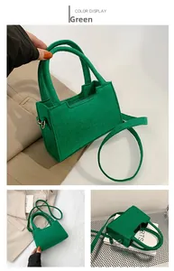 Detail view of a green felt crossbody bag with round handles and metal hardware