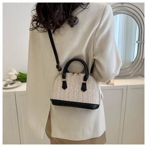 Détail d'un sac coquillage tissé beige avec garniture en cuir noir porté à l'épaule