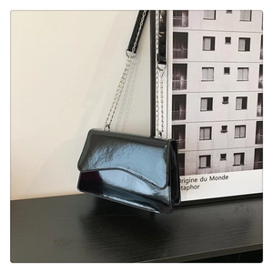 Detail of glossy black patent leather shoulder bag with wavy flap and silver chain strap