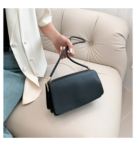 Detail of minimalist black rectangle shoulder bag with gold hardware on a leather sofa