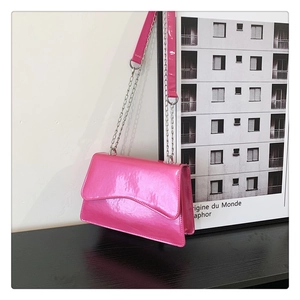 Detail of glossy pink patent leather crossbody bag with wavy flap and silver chain strap