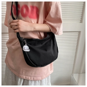 Detail of black canvas hobo bag with a cute white dog pendant worn as a crossbody bag
