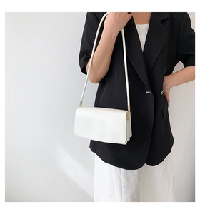 Minimalist white leather underarm bag with gold hardware shown on a model against a white wall
