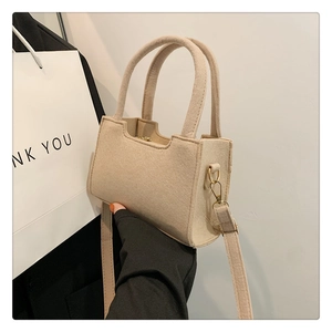 Close-up of minimalist cream felt handbag with round handles and gold hardware details