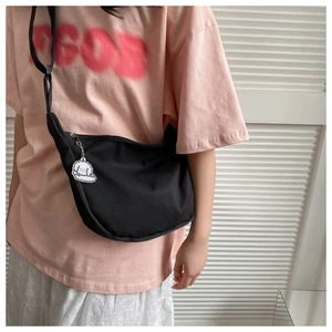Detailed view of black crescent crossbody bag with white puppy charm on female model