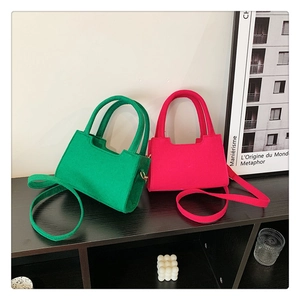 Detailed view of green and pink felt mini square handbags on a dark wooden shelf