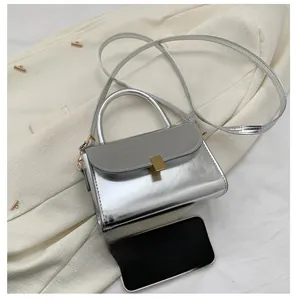 Detail view of mini silver mirror leather bag with gold hardware on fabric background