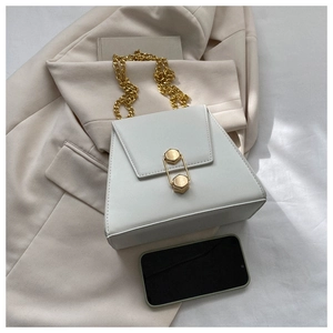 Sac à main en cuir blanc avec serrure hexagonale dorée et chaîne près d'un téléphone
