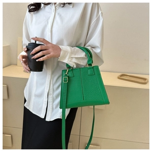 Detail of green crocodile embossed handbag featuring a top handle and gold hardware