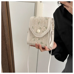 Detailed embroidery on a woven cream crossbody bag held by a model for size