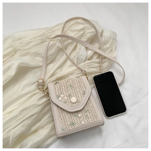 Detailed close-up of woven straw lace bag with green leaf embroidery and phone for scale