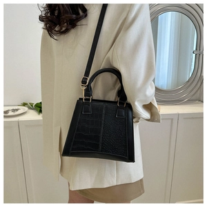 Detail view of black trapezoid handbag with embossed crocodile and pebble texture