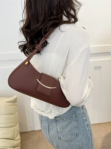 Brown leather underarm bag with gold buckle and twisted strap shown on shoulder