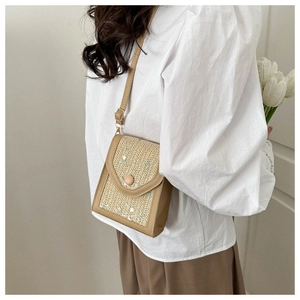 Detail of woven straw crossbody bag featuring white floral embroidery and magnetic closure