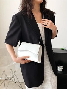 White minimalist crossbody bag with wavy flap design and silver chain on model