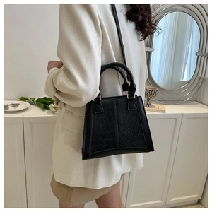 Detail of black trapezoid handbag with crocodile and pebble texture stitching in a room
