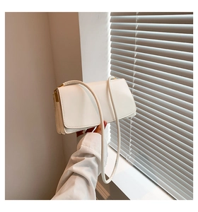 Detail of white leather underarm bag featuring a minimalist flap and gold metal accents