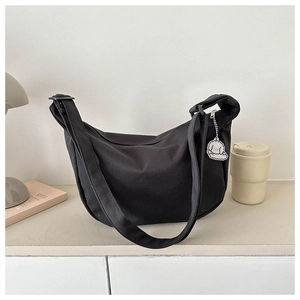 Close-up of black canvas crescent bag featuring a cute white plush puppy pendant