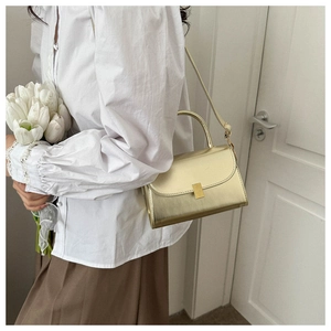 Detailed view of champagne gold crossbody bag with metallic finish and top handle on model