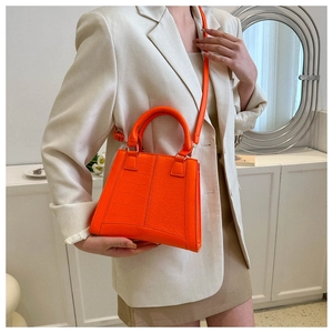 Detail of orange faux leather handbag featuring a crocodile pattern and crossbody strap