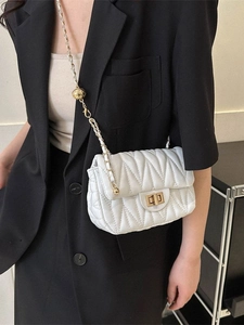 White quilted shoulder bag with gold chain and ball charm shown on a black suit jacket
