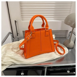 Detail of orange crocodile texture handbag with gold hardware on creative set