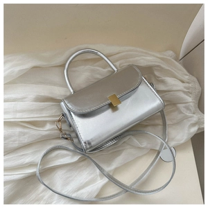 Close-up of silver metallic crossbody bag with golden buckle on soft white fabric