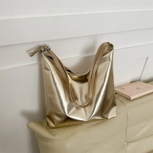 Metallic gold tote bag with dual shoulder straps resting on a minimalist white sofa