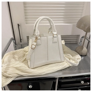 Detail of white crocodile pattern handbag with gold hardware and adjustable strap