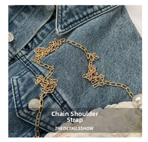 Detail of flat golden metal chain strap on white pleated bag with pearl embellishments