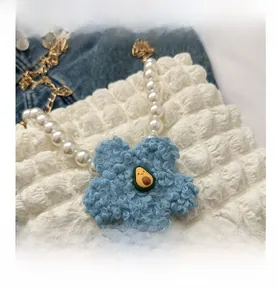 Detail of white pleated bubble bag with pearl handle and plush blue flower charm