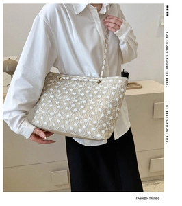 Dettaglio della borsa tote in paglia con ricamo in pizzo bianco e tracolla a catena dorata