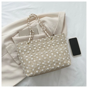 Dettaglio della borsa tote intrecciata beige con ricami floreali e tracolle a catena